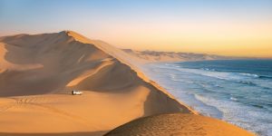 Car in the sand dunes and ocean view in Sandwich Harbour, Namib Naukluft Natural Park landscape in Namibia, Africa